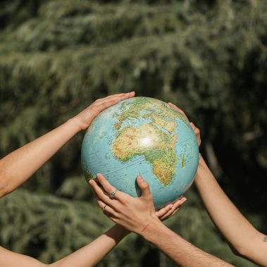 un globo terraquio con dos personas sosteniendo , solo se ve sus manos